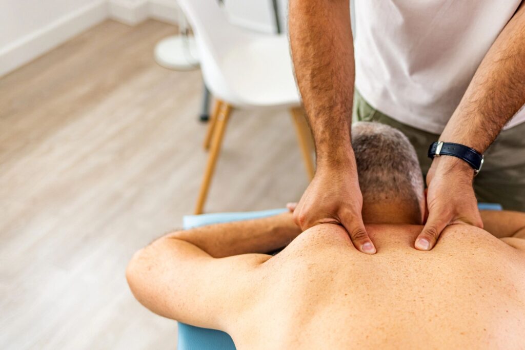 Physical therapist giving back massage to mature man. Patient lying down on massage table.